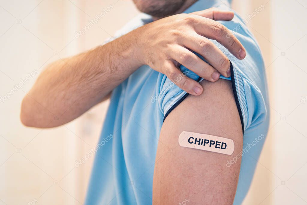 The concept of a conspiracy theory about chipping the world's population during mass vaccination against the covid 19 coronavirus. The shoulder is sealed with a band-aid with the inscription chipped.