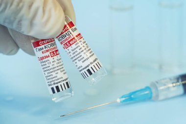 Koronovirüs enfeksiyonundan elde edilen Sputnik V aşısı mavi arka planda ve masada bir şırınga. 22 Temmuz 2021, Barnaul, Rusya.