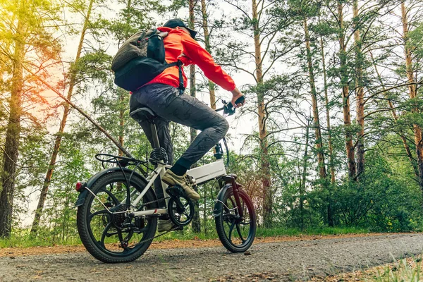 A cyclist rides on a bike path in the forest. Riding an electric modern bicycle. Cool fashionable bike with alloy wheels. A cyclist rides against the background of green trees