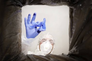 a man in a protective suit throws used medical glove into a trash can. Bottom view from the trash can. The problem of recycling and pollution of the planet with garbage. clipart