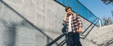 Telefonla konuşan modern yakışıklı genç adamın portresi. Elinde cep telefonu olan hippi bir adam. Şehir merdivenleri, şehir sokağı.