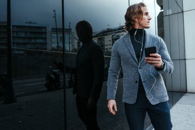 Şehir caddesinde elinde akıllı telefonuyla modern bir iş adamı. Yakışıklı adam kulaklık takıyor ve cep telefonuyla konuşuyor, müzik dinliyor ya da podcast yapıyor..