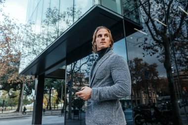 Şehir caddesinde elinde akıllı telefonuyla modern bir iş adamı. Yakışıklı adam kulaklık takıyor ve cep telefonuyla konuşuyor, müzik dinliyor ya da podcast yapıyor..