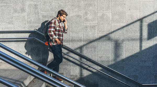 Portrait of modern handsome young man speaking on phone. Hipster guy with mobile in his hand outdoors. Urban stairs, city street