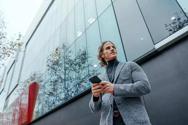 Şehir caddesinde elinde akıllı telefonuyla modern bir iş adamı. Yakışıklı adam kulaklık takıyor ve cep telefonuyla konuşuyor, müzik dinliyor ya da podcast yapıyor..