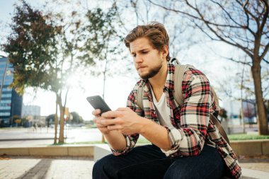 Sokakta akıllı telefonu olan modern bir gencin portresi. Elinde cep telefonu olan hippi bir adam.