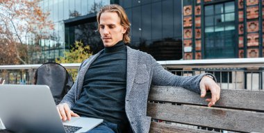 Dışarıda bankta otururken dizüstü bilgisayarda yazan yakışıklı genç adam. İş hayatı dengesi kavramı. Uzaktan çalışan işadamı serbest çalışan. Hipster blog yazıyor, internette sohbet ediyor, e-postaları kontrol ediyor.