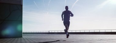 Genç ve zinde bir adam deniz kenarında koşuyor. Erkek koşucu sabah erkenden koşuyor. Sporcu dışarıda spor yapıyor. Spor salonunun dışındaki kilitlenme sırasında egzersiz..