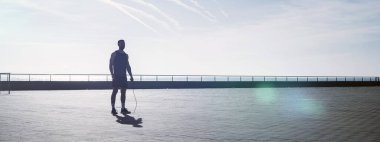 Zinde genç bir adam dışarıda ip atlıyor. Erkek sporcu sabahları spor yapıyor. Spor salonunun dışındaki kilitlenme sırasında egzersiz..