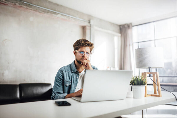 Young man typing on laptop. Modern businessman at sunny office. Freelancer at work. Blogger or journalist writing new article