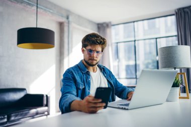 Akıllı telefonu elinde daktilo eden genç bir adam. Güneşli ofisteki modern iş adamı. Serbest İşçi.