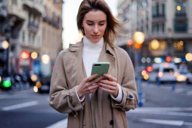 Gece sokakta akıllı telefon kullanan genç bir kadın.