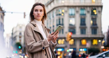 Gece sokakta akıllı telefon kullanan genç bir kadın.