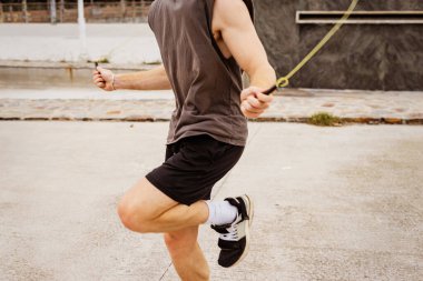 Kaslı genç adam dışarıda ip atlamakla egzersiz yapıyor.