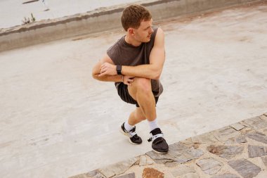 Genç atletik çocuk antrenman yapıyor. Spor salonu açık havada. Esniyorum. Şehir arkaplanı.
