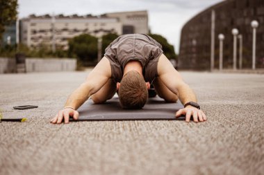 Genç atletik çocuk antrenman yapıyor. Spor salonu açık havada. Esniyorum. Şehir arkaplanı.