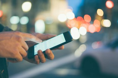 Şehir caddesinde gece vakti akıllı telefonlu erkeklerin internet ya da sosyal ağları ararken, hipster bir mesajla ya da mesajla sohbet ederken görüntüsü.