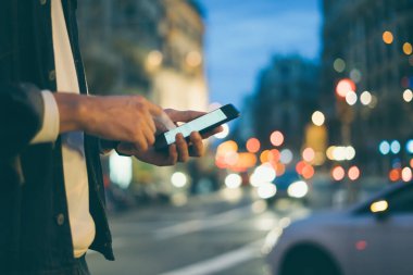 Şehir caddesinde gece vakti akıllı telefonlu erkeklerin internet ya da sosyal ağları ararken, hipster bir mesajla ya da mesajla sohbet ederken görüntüsü.