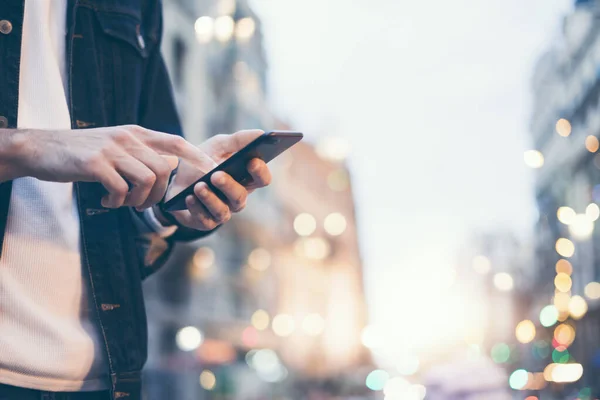 Şehir caddesinde gece vakti akıllı telefonlu erkeklerin internet ya da sosyal ağları ararken görüntüsü, hipster sohbet üzerine bir SMS mesajı yazıyor, bokeh ışıkları