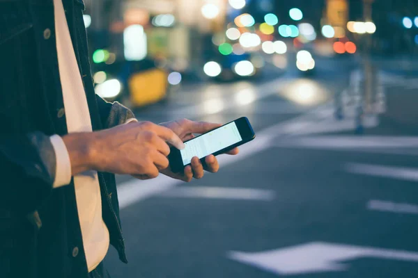 Closeup image of male hands with smartphone at night on city street, searching internet or social networks, hipster man typing an sms or message on chat, bokeh lights