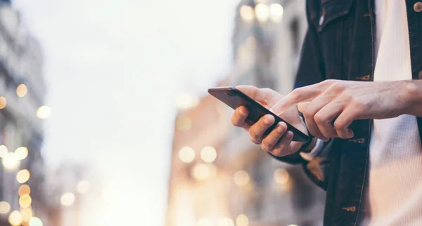 Şehir caddesinde gece vakti akıllı telefonlu erkeklerin internet ya da sosyal ağları ararken görüntüsü, hipster sohbet üzerine bir SMS mesajı yazıyor, bokeh ışıkları