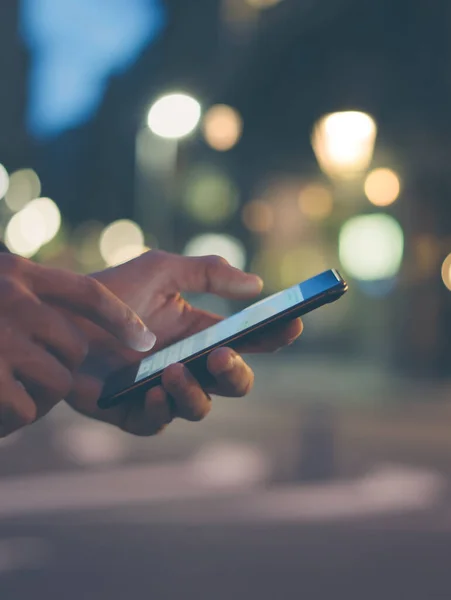 Şehir caddesinde gece vakti akıllı telefonlu erkeklerin internet ya da sosyal ağları ararken, hipster bir mesajla ya da mesajla sohbet ederken görüntüsü.