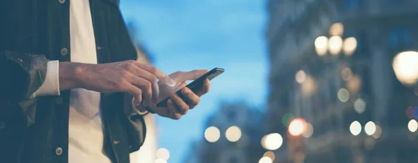 Şehir caddesinde gece vakti akıllı telefonlu erkeklerin internet ya da sosyal ağları ararken görüntüsü, hipster sohbet üzerine bir SMS mesajı yazıyor, bokeh ışıkları