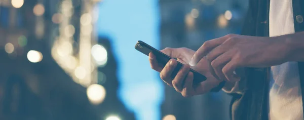 Şehir caddesinde gece vakti akıllı telefonlu erkeklerin internet ya da sosyal ağları ararken görüntüsü, hipster sohbet üzerine bir SMS mesajı yazıyor, bokeh ışıkları
