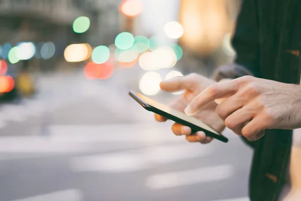 Şehir caddesinde gece vakti akıllı telefonlu erkeklerin internet ya da sosyal ağları ararken görüntüsü, hipster sohbet üzerine bir SMS mesajı yazıyor, bokeh ışıkları