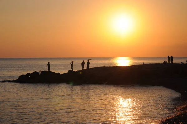Gün batımında deniz kıyısındaki insanların siluetleri