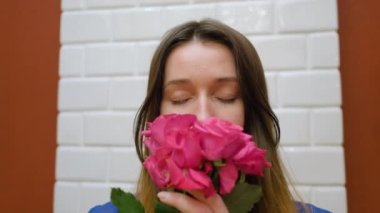 Güzel kahverengi saçlı kadın yüzüne pembe güller getiriyor ve aromalarını zevkle içine çekiyor, yakın çekim, yavaş çekim.