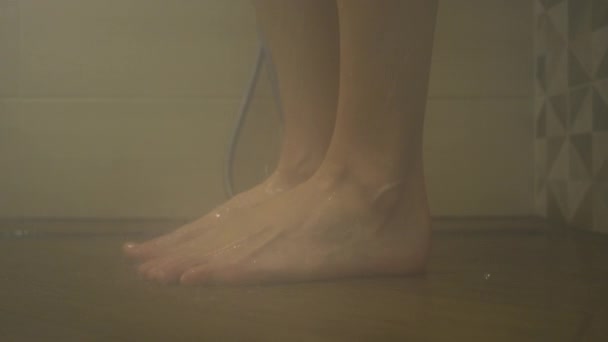 Piedi femminili sotto la doccia dietro vetro su una piastrella. cadute d'acqua, sudorazione di vetro, primo piano, al rallentatore — Video Stock