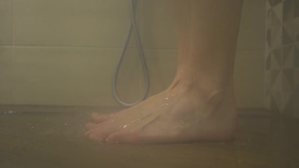 De pie a pie en la ducha detrás del vidrio, de pie sobre las baldosas. Tome una ducha detrás del vidrio, de cerca, en cámara lenta — Vídeo de stock