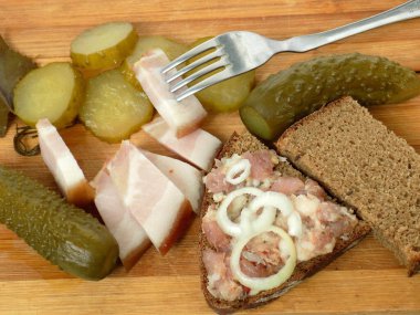 Basit aperatif: pastırmalı sandviç, soğan halkaları, bir dilim ekmek ve salatalık turşusu.