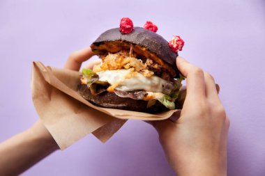 Corona (antiCOVID) çizburger, insan yapımı siyah çörek, marul, kızarmış soğan ve peynirli menekşeli menekşe arkaplan. Restoran, burger barı. Yatay görünümü kapat.