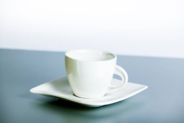 Kahve fincanı ve çay tabağı gri bir masada, beyaz bir duvara karşı. Kahve molası, dinlenme. Yakın plan.. 