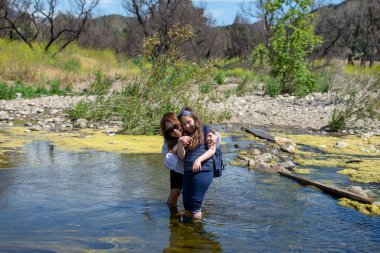 Bahar aylarında bir derede ya da nehirde oynarken ayakta duran ve gülen kadın ve kız.