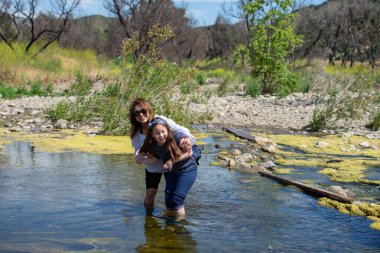 Bahar aylarında bir derede ya da nehirde oynarken ayakta duran ve gülen kadın ve kız.