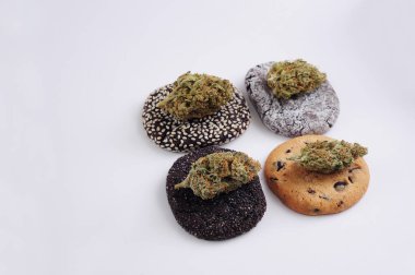 Kurabiyeler ve marihuana tomurcukları yakın plan. Beyaz arka planda kenevir çiçekleri ve tatlılar. Kenevir rekreasyonu, eğlence, yasallaştırma konsepti. 