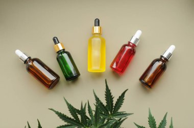 Kenevir cbd yağı ve gri arka planda yeşil yapraklar. Kozmetolojide marihuana özü.