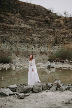 Güzel genç gelin kayaların üzerinde duruyor ve gölde poz veriyor.
