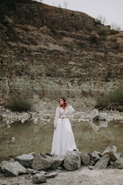Güzel genç gelin kayaların üzerinde duruyor ve gölde poz veriyor.