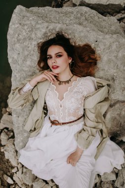 Tepeden bakan çekici kadın kayanın üzerinde yatıyor. 