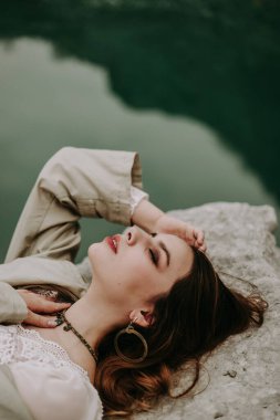 Tepeden bakan çekici kadın kayanın üzerinde yatıyor. 
