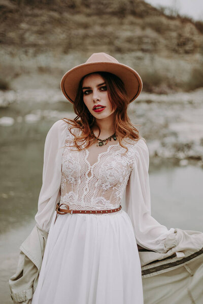 beautiful young woman in a hat and a white dress in the mountains 