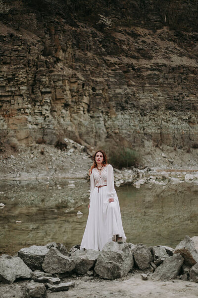 Beautiful young woman in white dress posing on the rocks in the lake