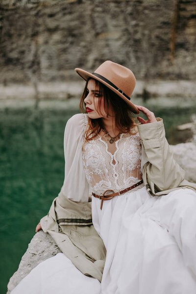 portrait of lady in a white dress posing on rock at lake 