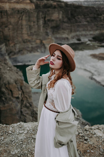 young woman in a white dress standing on rock with river on background 