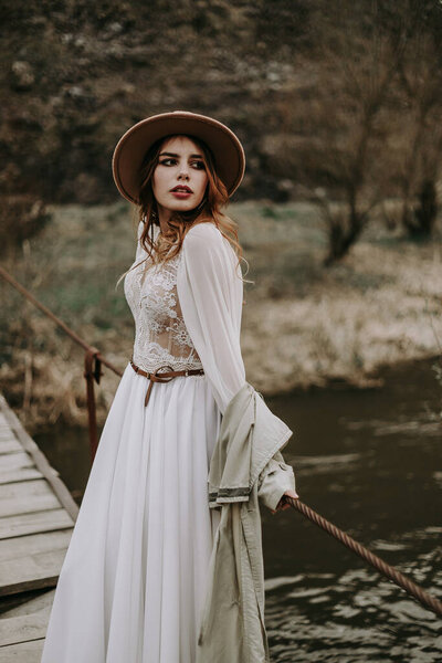  young woman in a hat standing on wooden bridge over the river 