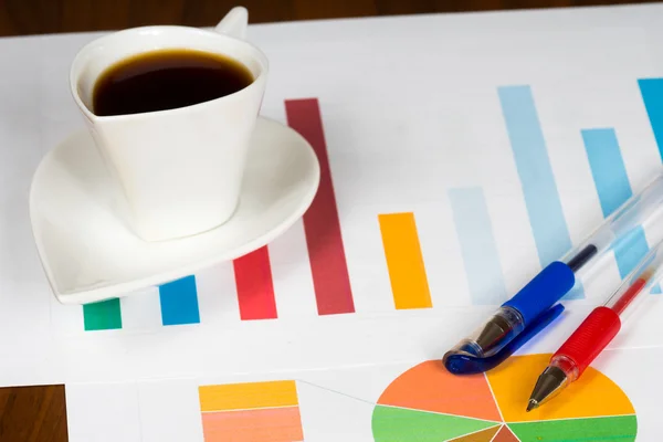 Tazza di caffè con bar colorato e grafici a torta e penne — Foto Stock